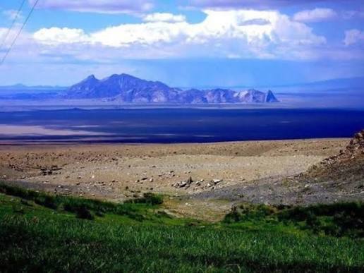 Eej Khairkhan mountain across a wide desert plain with green vegetation in the foreground.