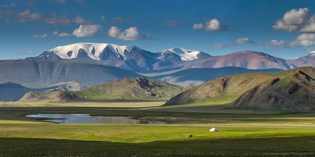 Snow-covered Tsambagarav peaks above a green valley, small pools and a white ger.