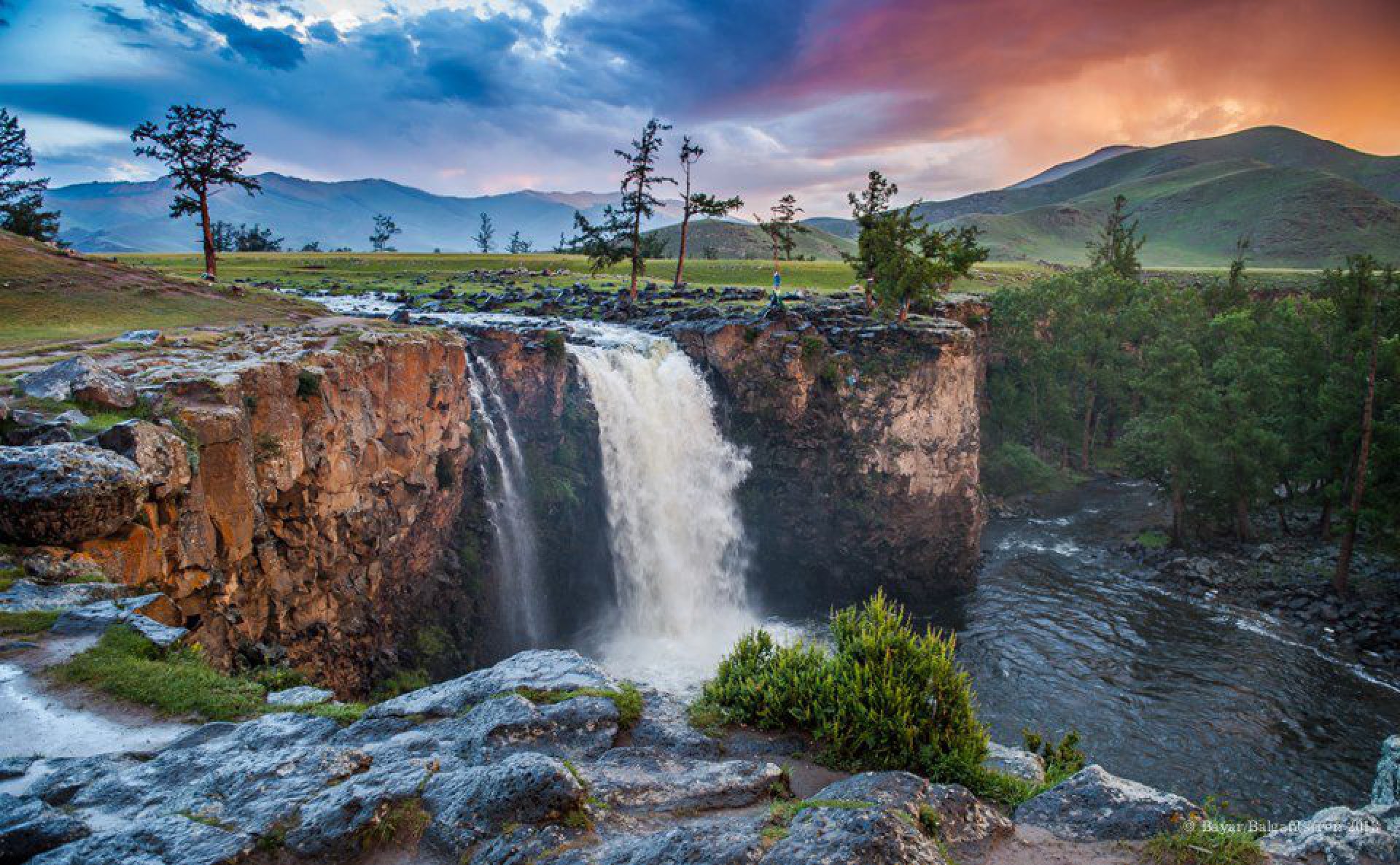 Ulaan Tsutgalan Waterfall cascading into a rocky gorge beneath a colourful sky.