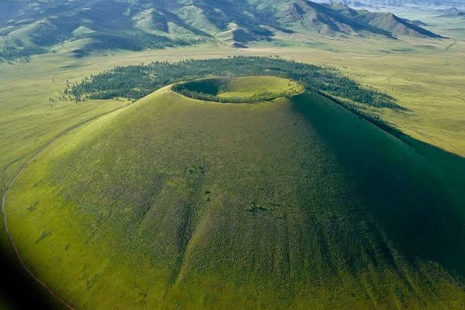 Aerial view of Uran Togoo’s grassy volcanic cone, circular crater and surrounding woodland.